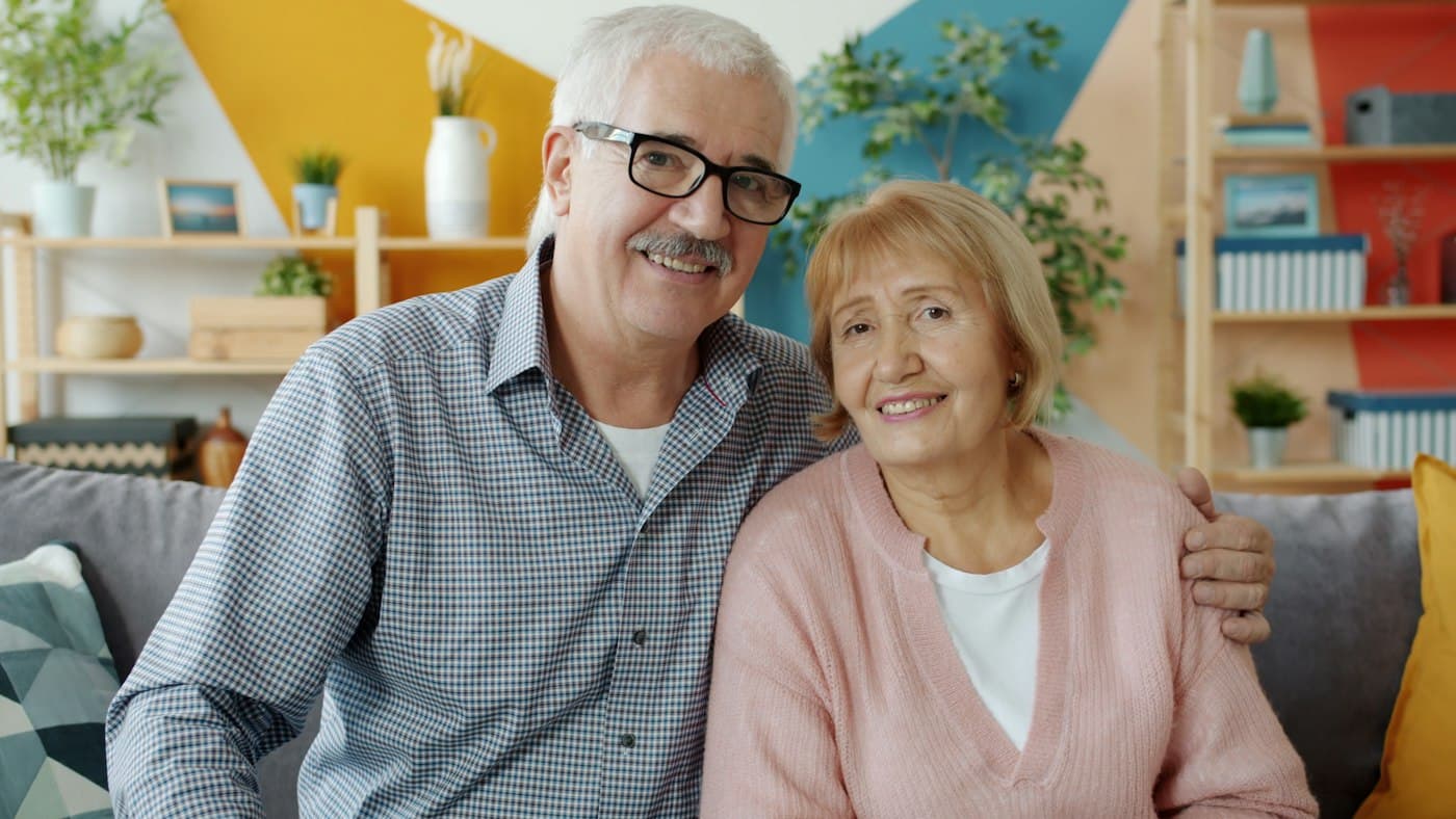 Couple de retraités souriant, assis dans leur salon