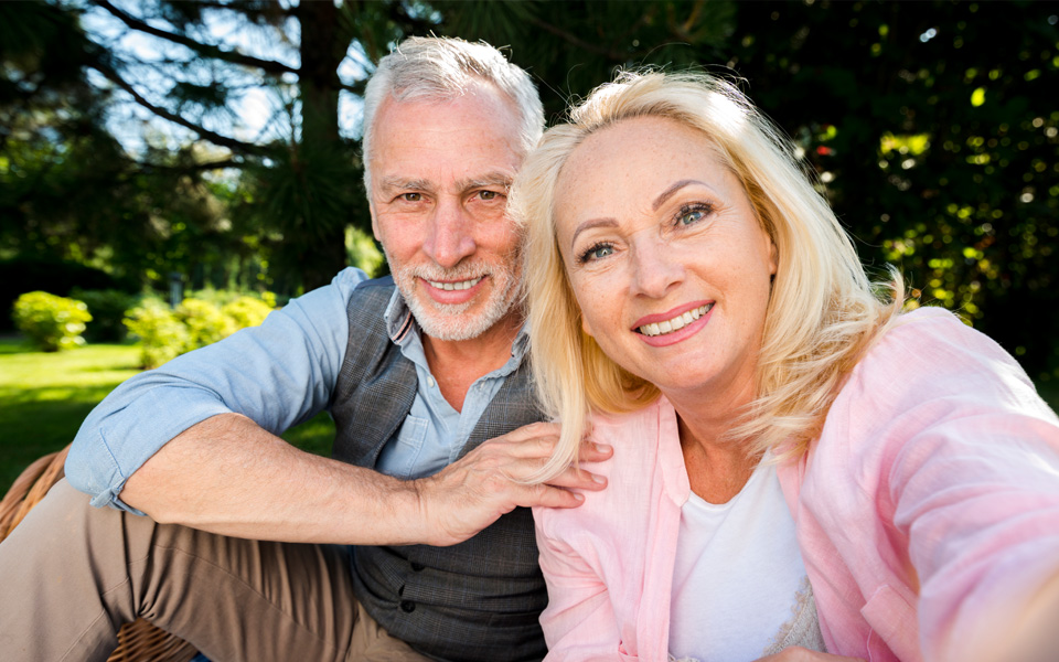 Deux seniors assis dans un jardin, prenant un selfie ensemble