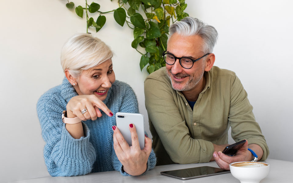 Deux seniors, une femme et un homme, souriants tout en utilisant leur téléphone portable